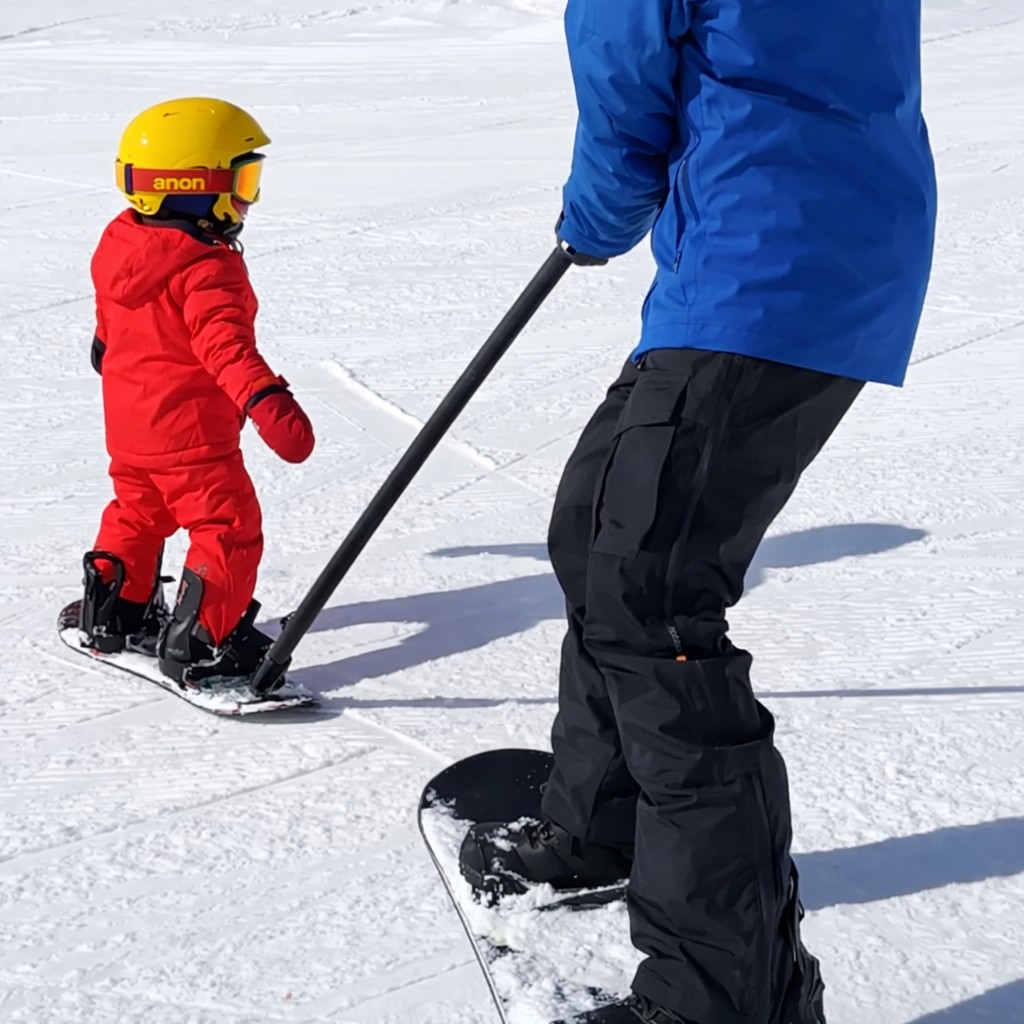 Young child snowboarding with Snowmigo guide pole