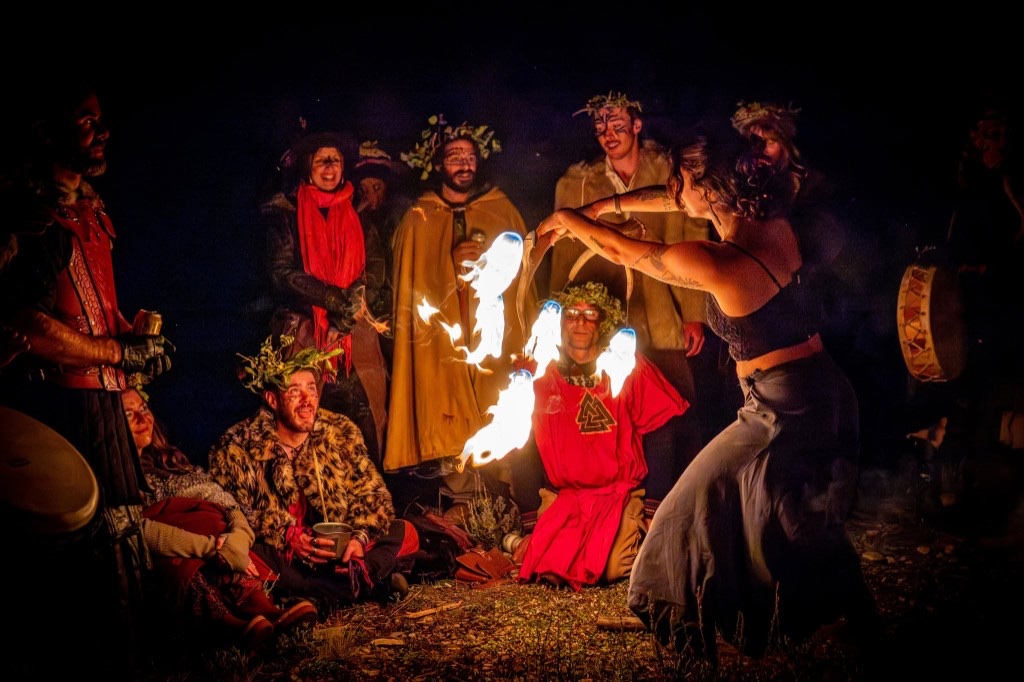 Fire performer and costumed community circle at night during Vinotok — leaf crowns, ritual dress, and firelight
